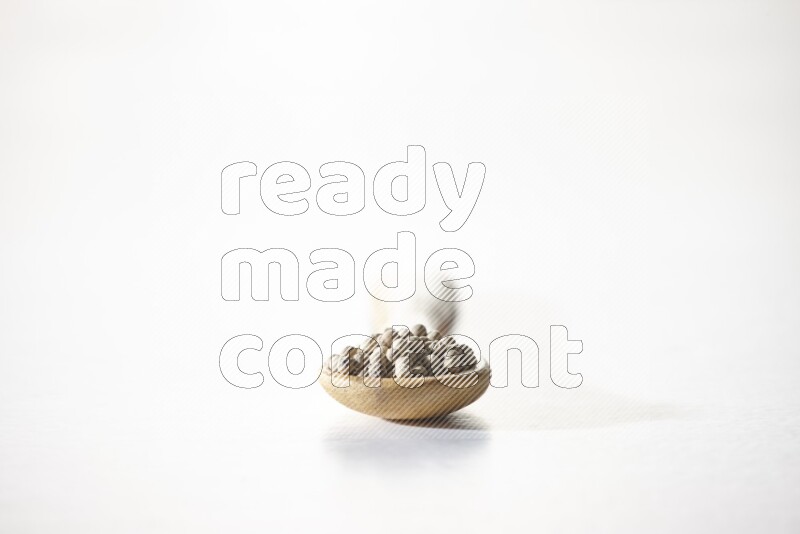 A wooden spoon full of white pepper beads on white flooring