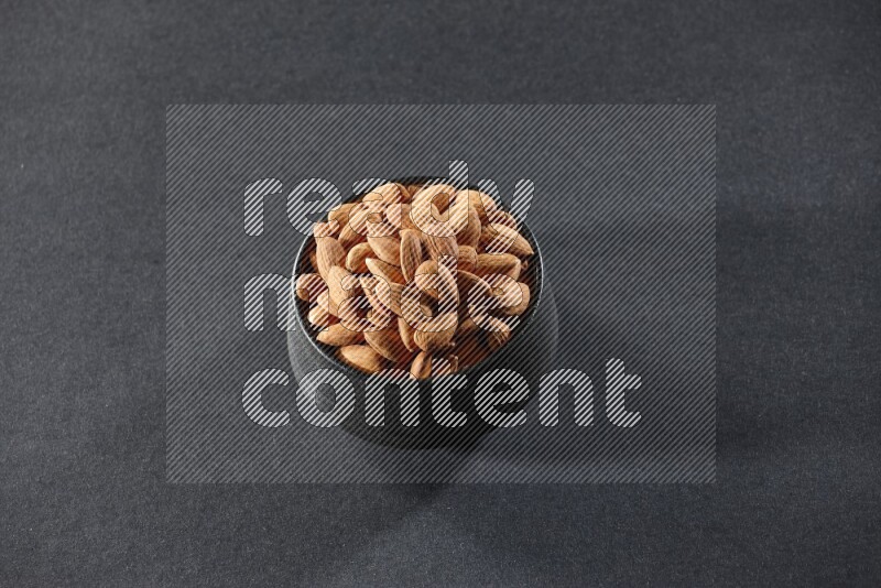 A black pottery bowl full of peeled almonds on a black background in different angles