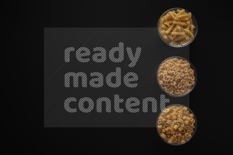 Different pasta types in 3 glass bowls on black background