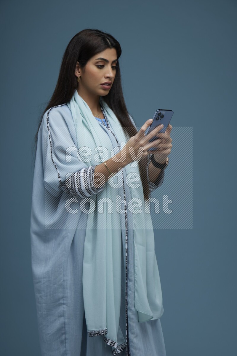 A Saudi woman Texting in a blue background wearing blue Abaya with no hijab