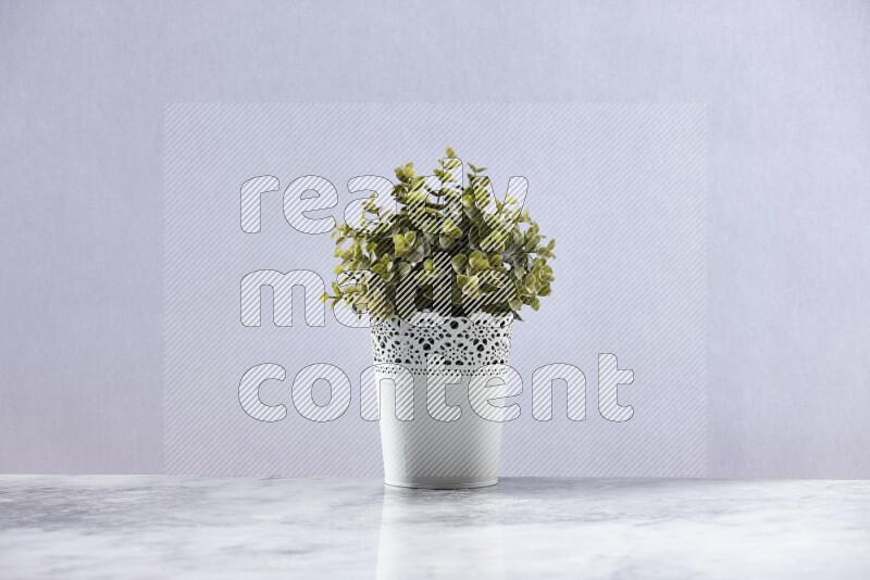 Green artificial plant in white decorative pot on grey marble background