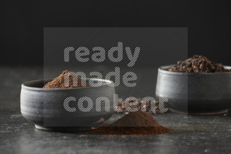 وعاءين من الفخار الأسود أحدهما ممتلئي بحبوب القرنفل والآخر ممتلئ ببودرة القرنفل على خلفية سوداء