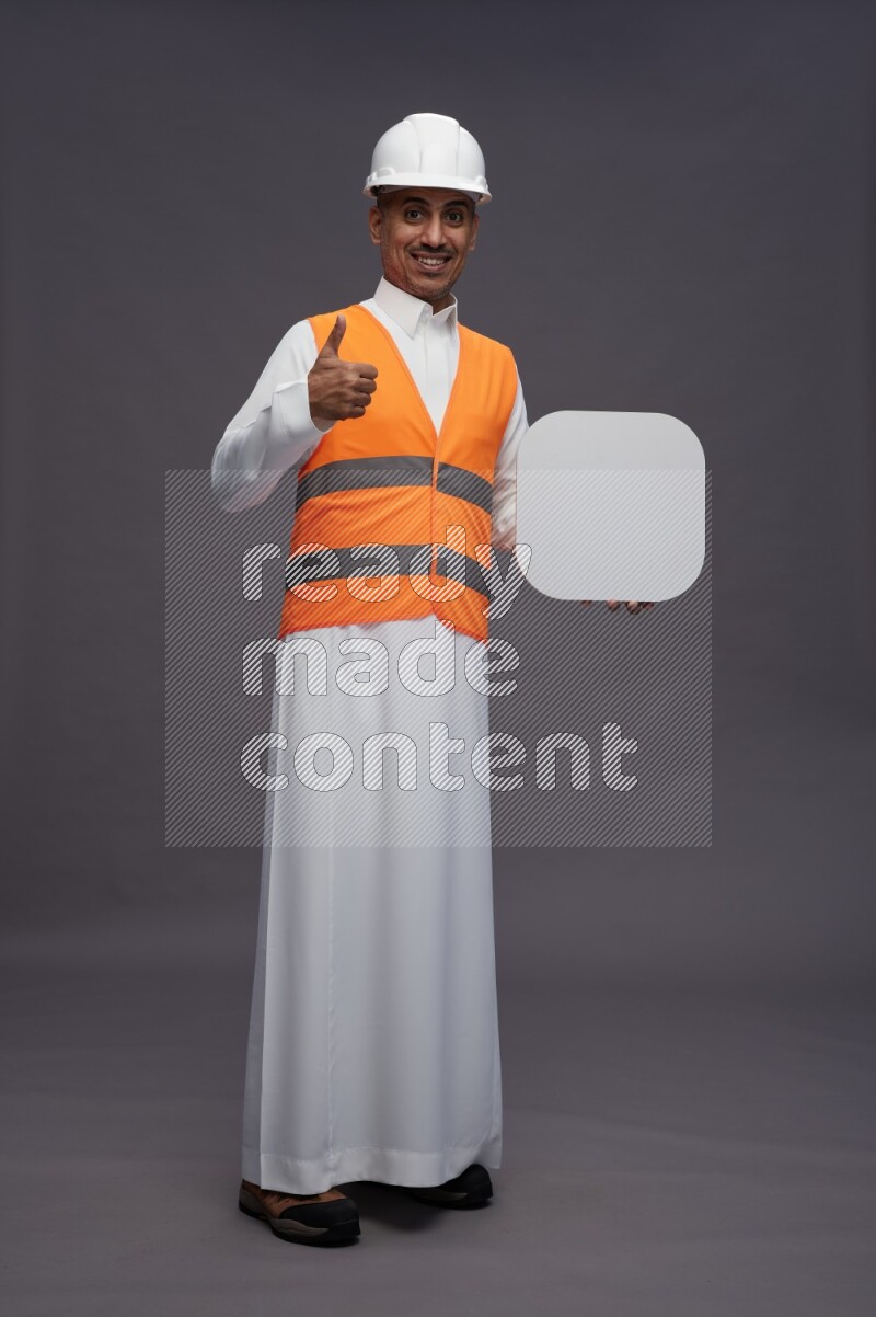 Saudi man wearing thob with engineer vest standing holding social media sign on gray background