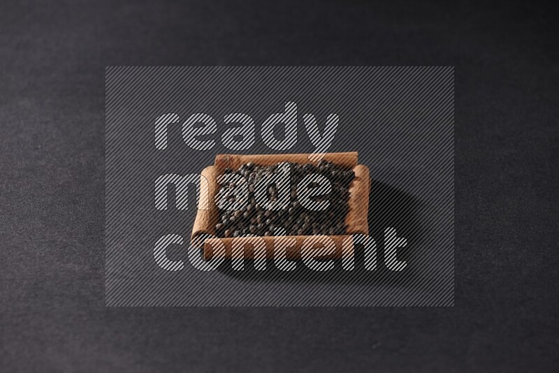 A single square of cinnamon sticks full of black pepper on black flooring