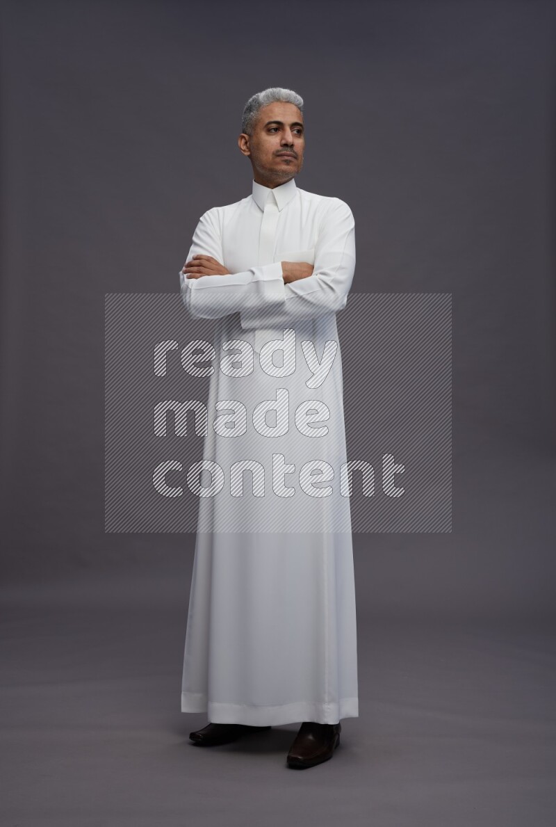 Saudi man wearing thob standing with crossed arms on gray background