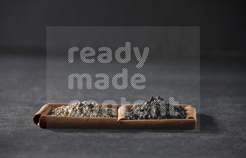 2 squares of cinnamon sticks full of white peppers and black peppers on black flooring