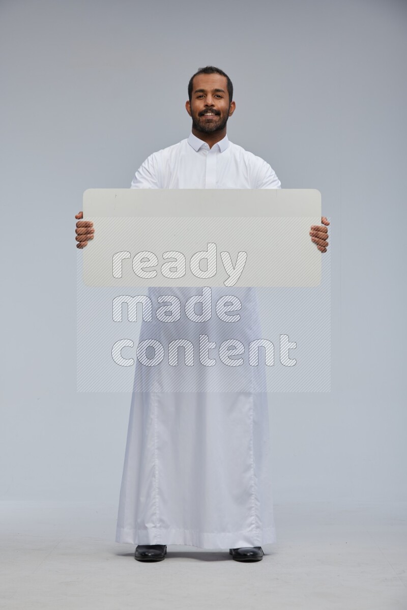 Saudi man wearing Thob standing holding board on Gray background
