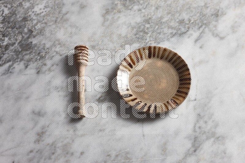 Multicolored pottery plate with wooden honey dipper on the side on grey marble background