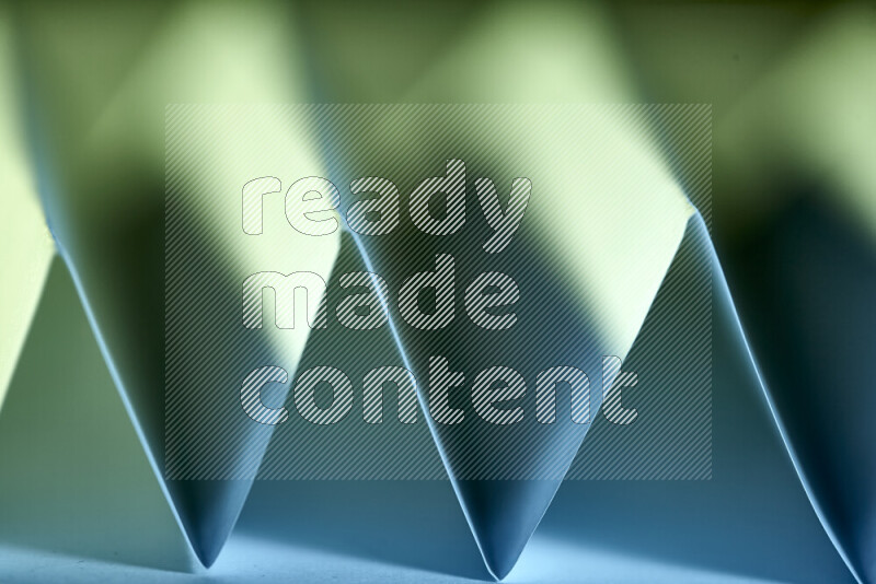 A close-up abstract image showing sharp geometric paper folds in green and blue gradients