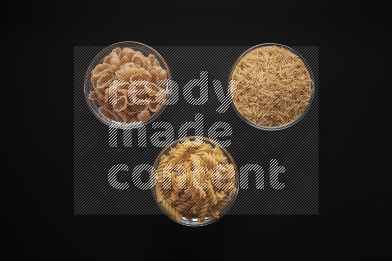 Different pasta types in glass bowls on black background