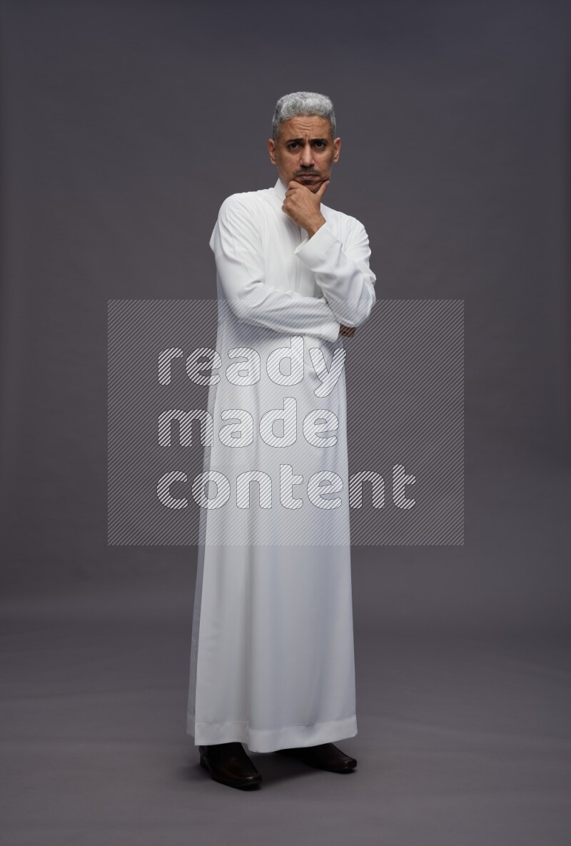 Saudi man wearing thob standing interacting with the camera on gray background