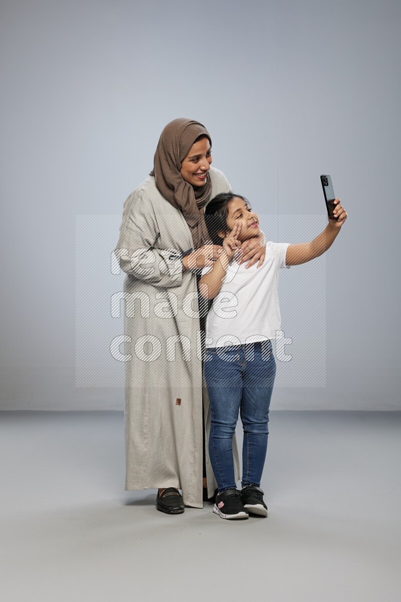 A girl standing taking selfie with her mother on gray background