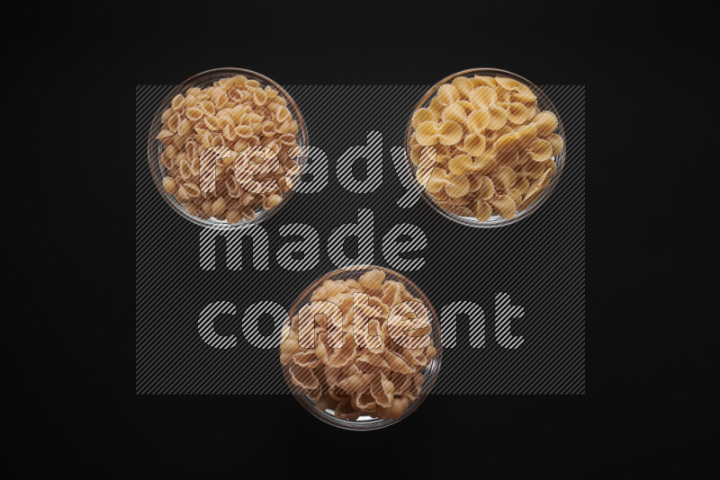 Different pasta types in glass bowls on black background