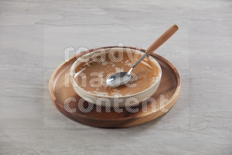 multi color pottery round dish on top of brown wood round plate and spoon, on grey textured countertop