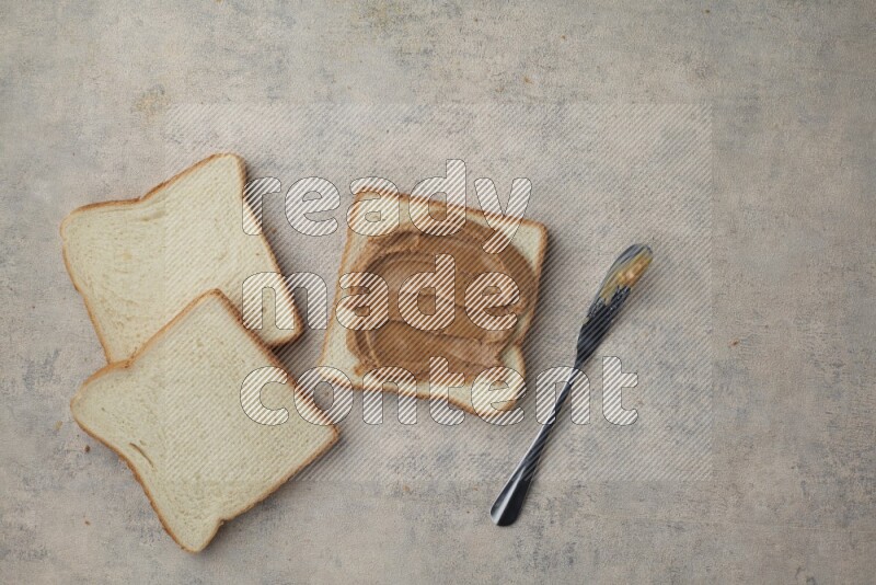 Creamy peanut butter on white toast and white toast slices on a light blue textured background