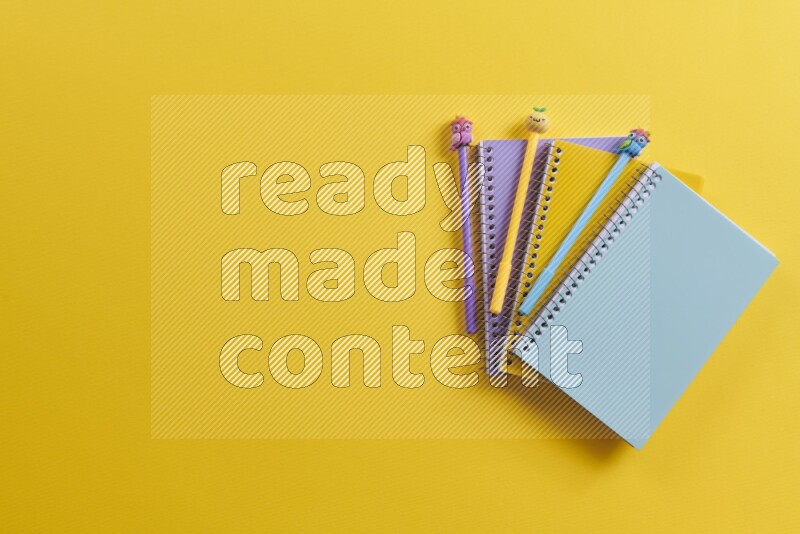 Multicolored notebooks with school supplies on yellow background