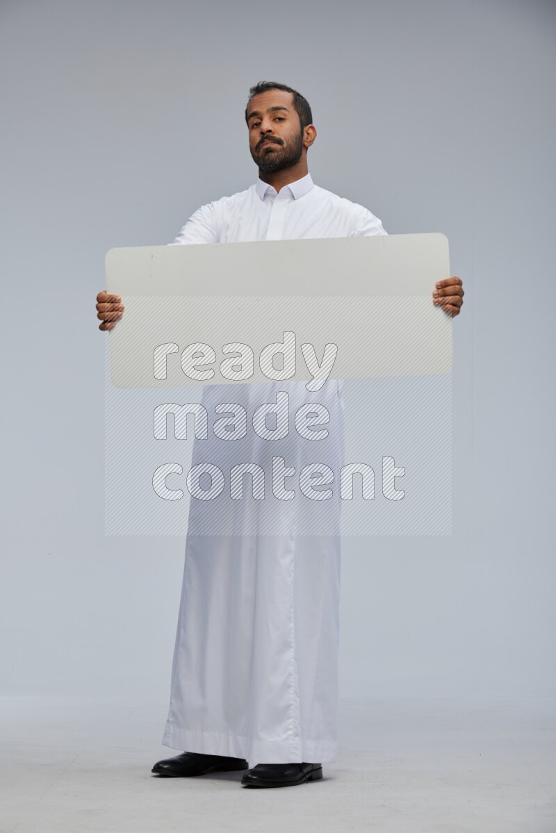 Saudi man wearing Thob standing holding board on Gray background