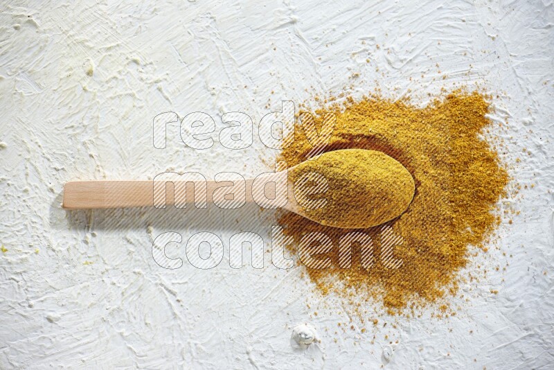 A wooden spoon full of turmeric powder on textured white background