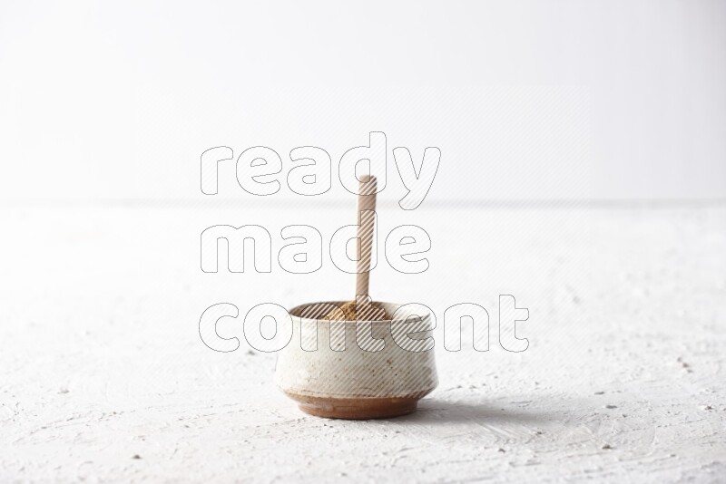 Ceramic beige bowl full of cinnamon powder with a wooden spoon on a textured white background