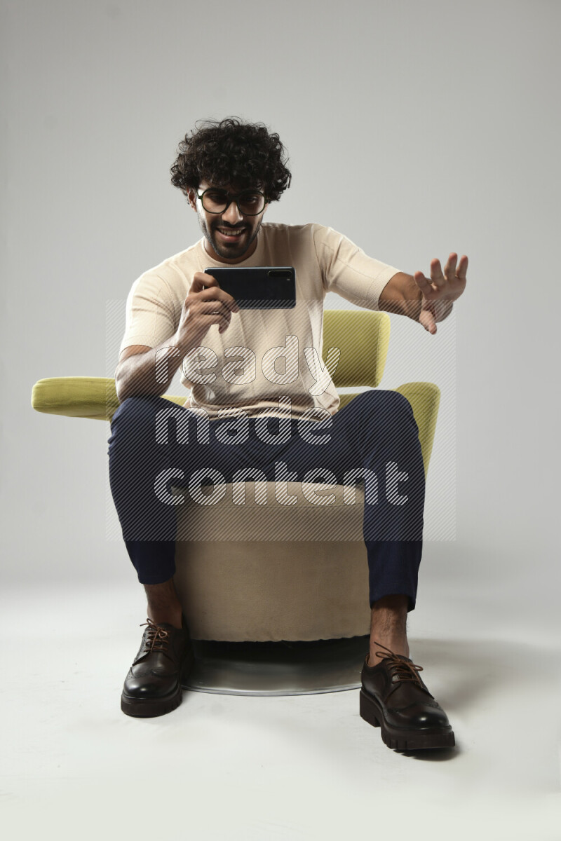 A man wearing casual sitting on a chair shooting with his phone on white background