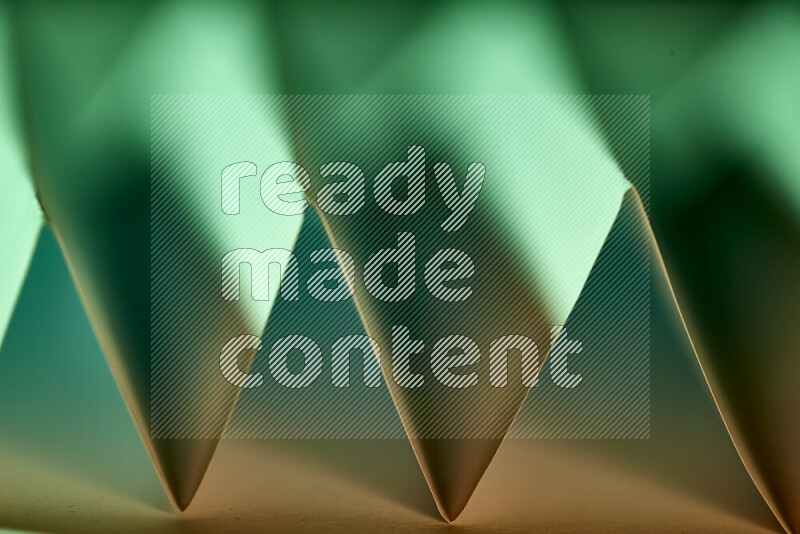 A close-up abstract image showing sharp geometric paper folds in green gradients and warm tones