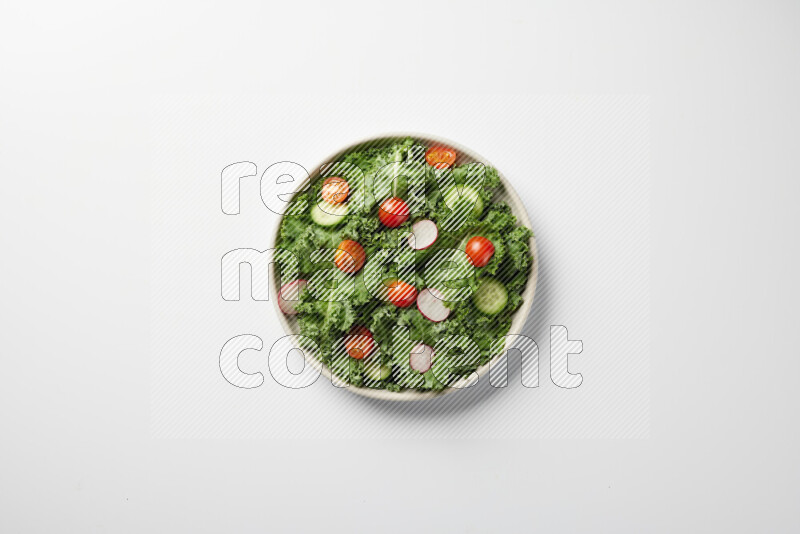 A bowl of fresh vegetables salad with kale leaves, cherry tomatoes, sliced radishes and sliced cucumber on a white background