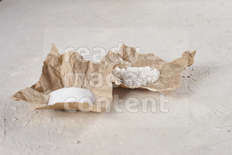 A crumpled piece of paper full of white salt on white background