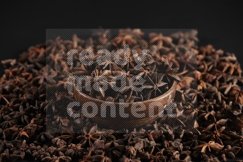 Star Anise in a wooden bowl and surrounded by more anise filling the frame on black flooring