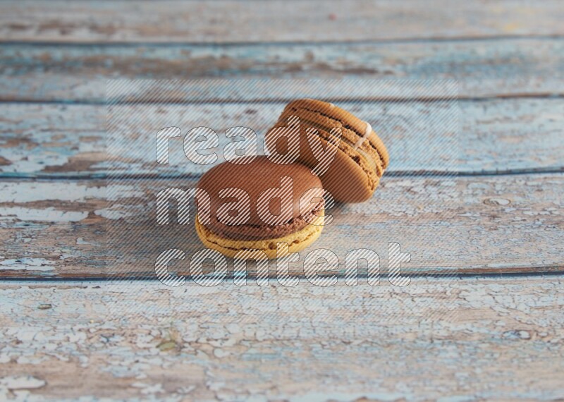 45º Shot of of two assorted Brown Irish Cream, and Yellow, and Brown Chai Latte macarons  on light blue background