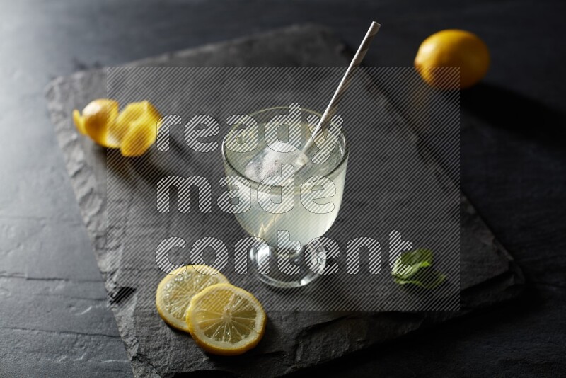 A glass of lemon juice with a straw on black background