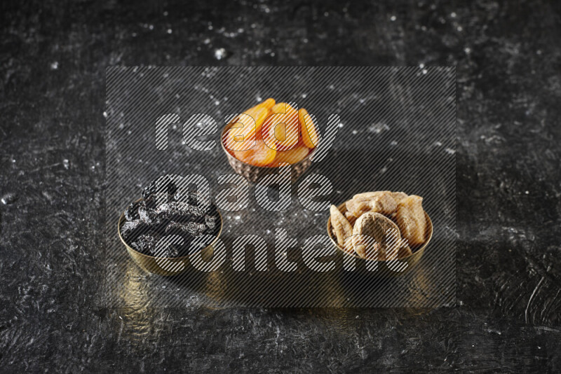 Dried fruits in metal bowls in a dark setup