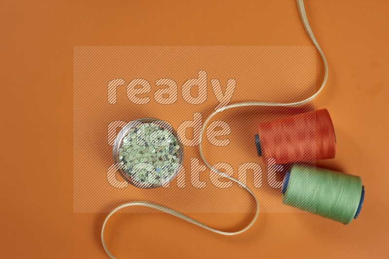 A green and orange collection of sewing and tailoring tools arranged on a orange background