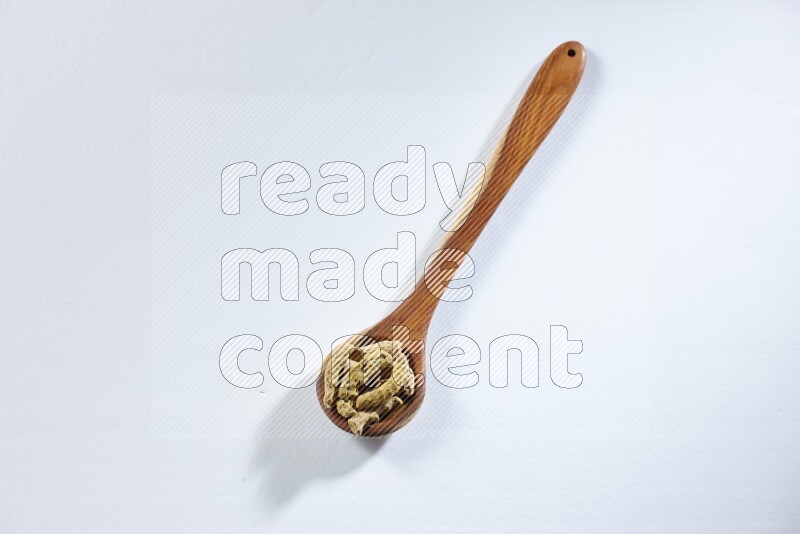 A wooden ladle full of dried turmeric fingers on white flooring