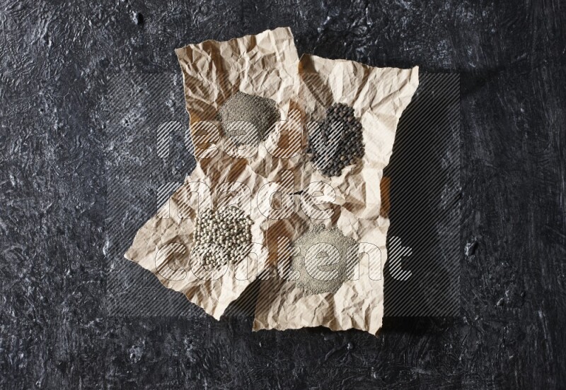 Crumpled pieces of paper full of black and white pepper beads and powder on a textured black flooring