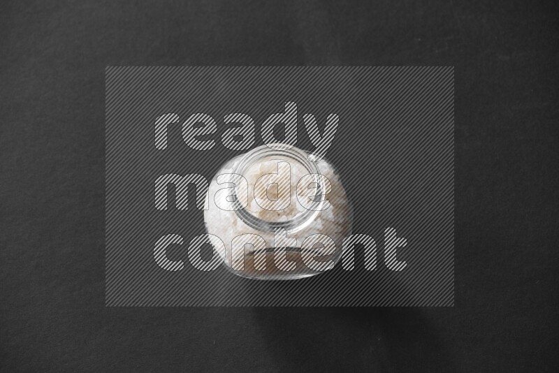 A glass spice jar full of salt on black flooring