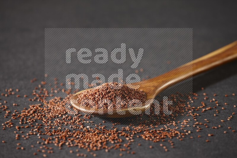 A wooden ladle full of garden cress seeds and seeds spread beside it on a black flooring