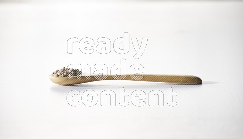 A wooden spoon full of white pepper beads on white flooring