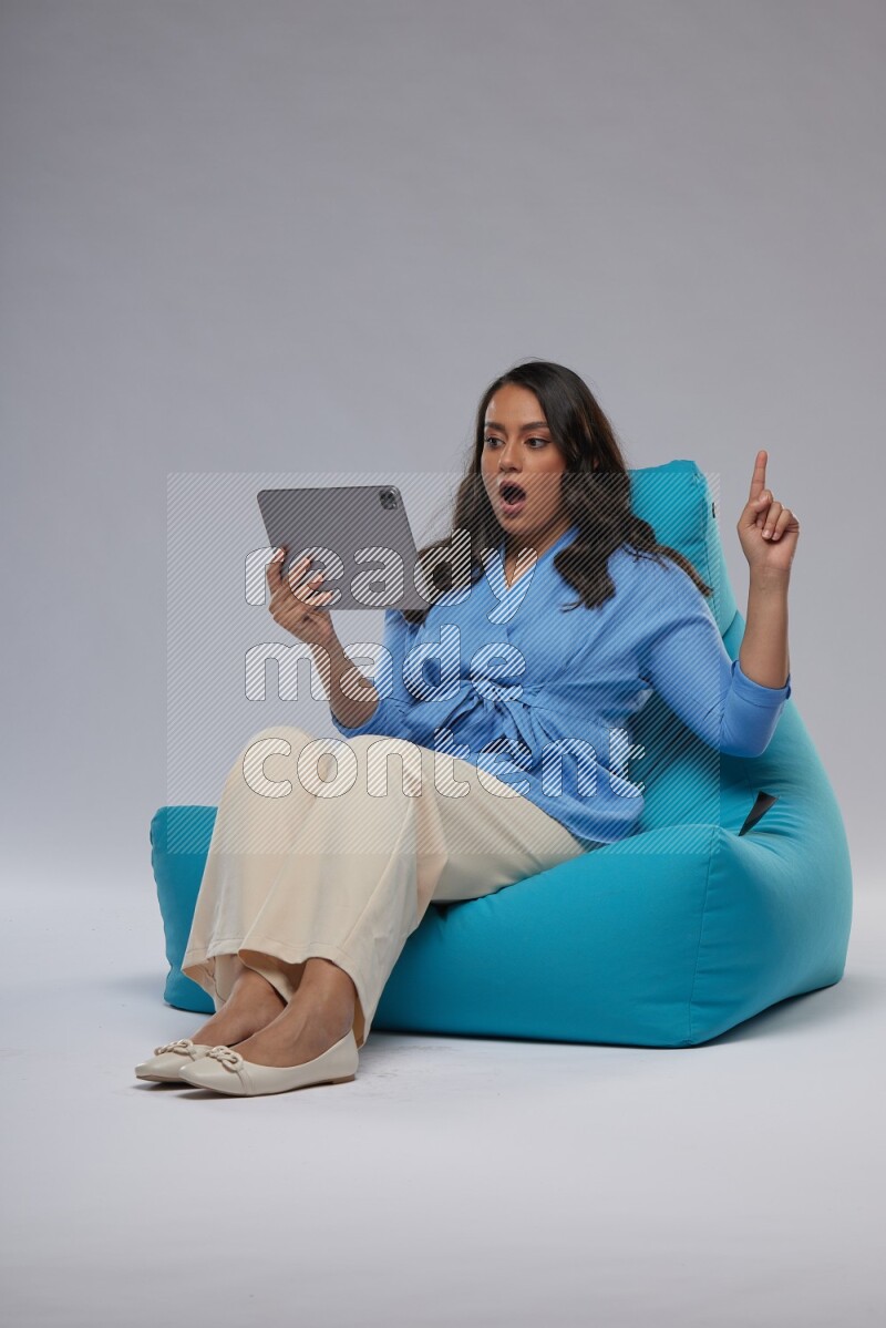 A woman sitting on a blue beanbag and working on tablet