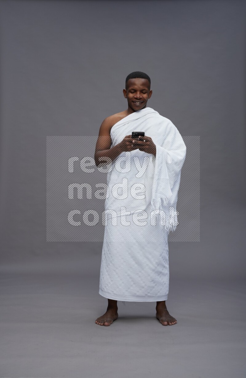 A man wearing Ehram Standing texting on phone on gray background