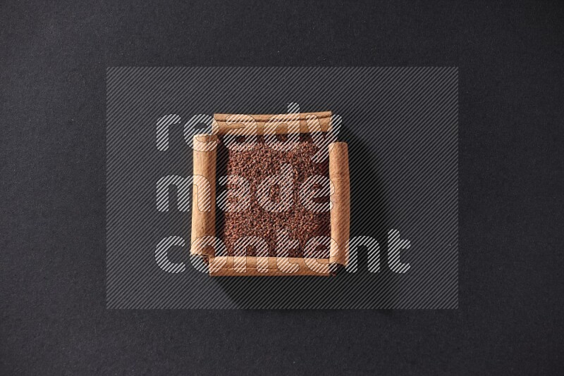 أربعة من أعواد القرفة مكونة شكل مربع بداخلها حب الرشاد علي خلفية سوداء