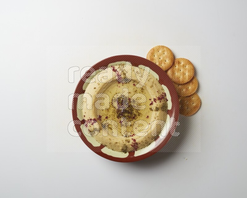 Hummus in a traditional plate garnished with zaatar & sumak on a white background