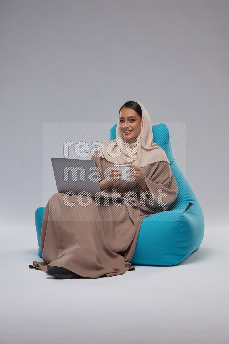 A Saudi woman sitting on a blue beanbag and working on laptop