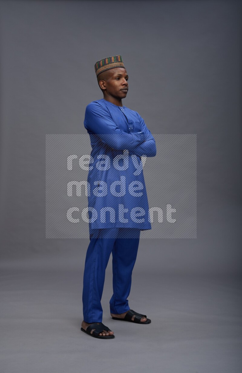 Man wearing Nigerian outfit standing with crossed arms on gray background