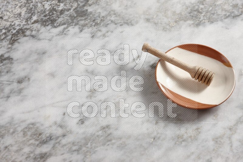 Multicolored pottery plate with wooden honey dipper in it on grey marble background