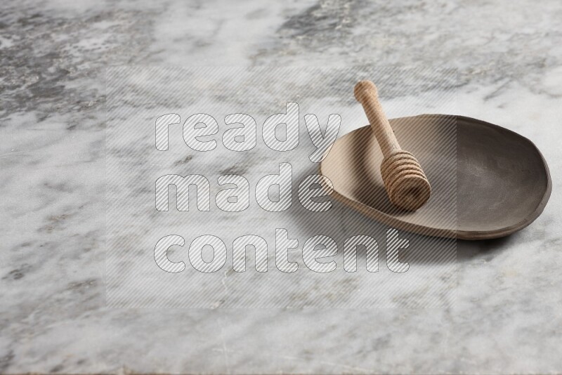 Multicolored pottery plate with wooden honey dipper in it on grey marble background