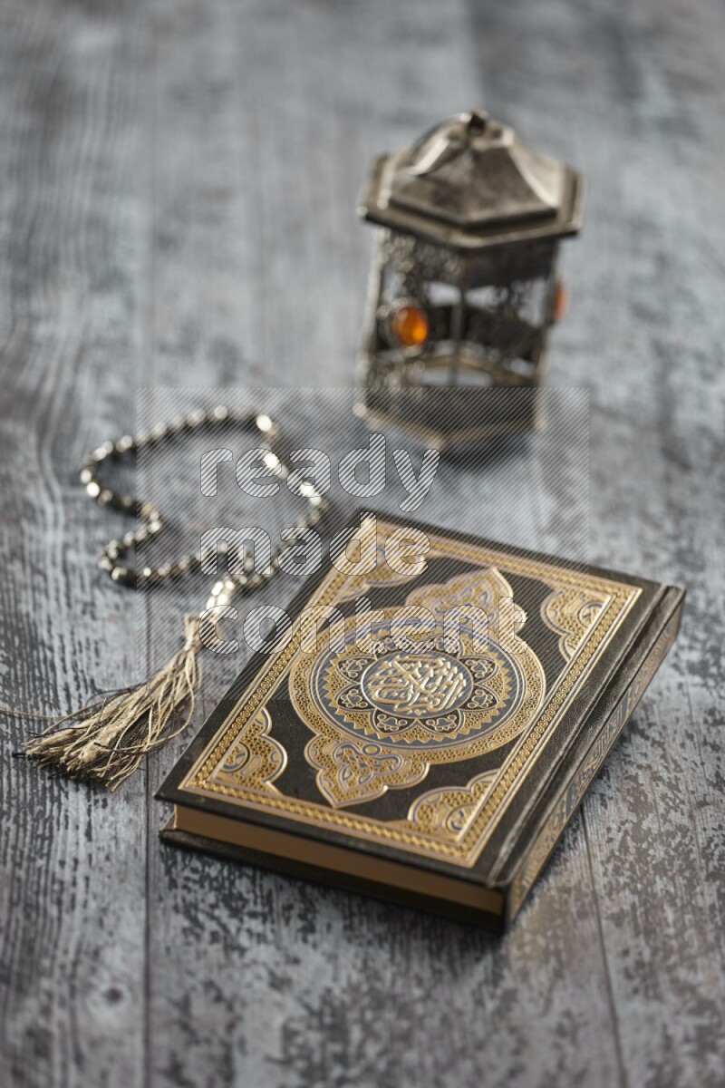 A silver lantern with different drinks, dates, nuts, prayer beads and quran on grey wooden background