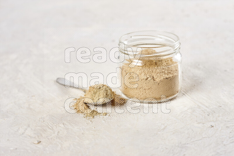 A glass jar full of ground ginger powder on white background