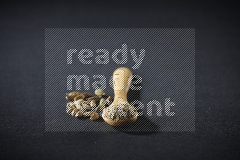 ملعقة خشبية ممتلئة ببودرة الهيل وحبوب الهيل بجانبها على خلفية سوداء