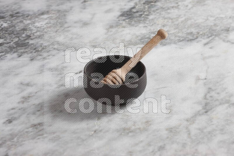 Black pottery bowl with wooden honey dipper in it on grey marble background