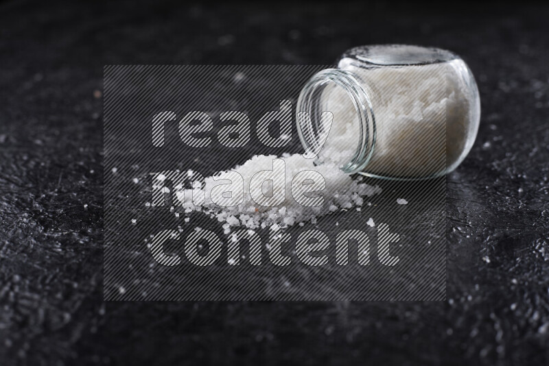 A glass jar full of coarse sea salt crystals on black background